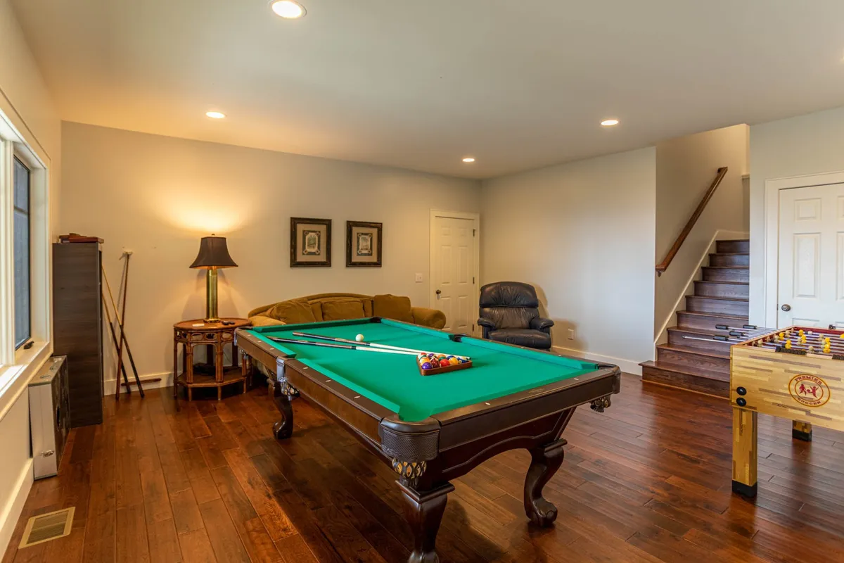 This image captures a vibrant game room setting with a pool table, foosball table, sofa, and wall art. The space feels casual and inviting—ideal for socializing and family game nights. The lighting and comfortable furnishings add to the warm, friendly atmosphere.