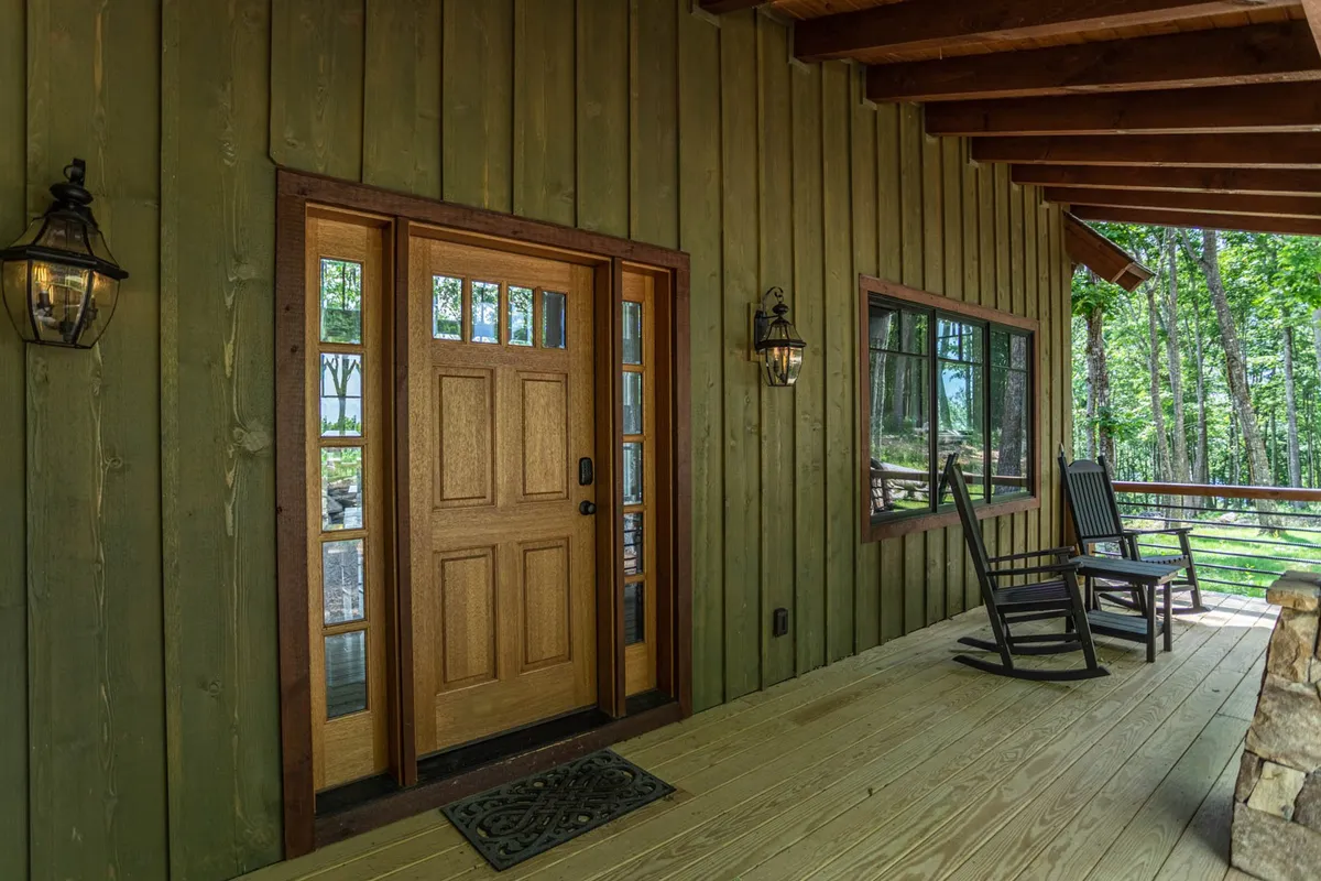 A welcoming front door with a rocking chair and lanterns on a cozy porch, framed by windows and greenery. The porch embodies a warm, friendly atmosphere and connects indoor comfort with the surrounding nature.