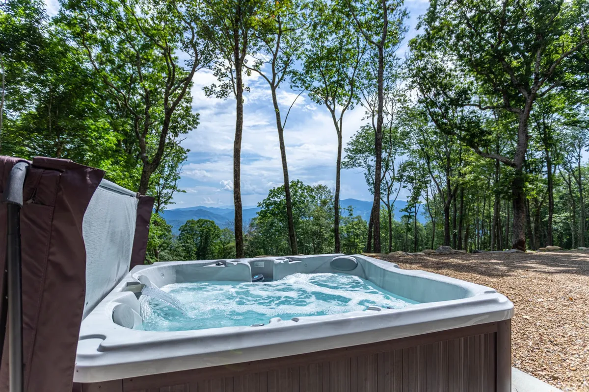An outdoor hot tub is set amidst surrounding trees with a striking mountain view in the background. The setting is tranquil and perfect for relaxing, socializing, or stargazing under the night sky.