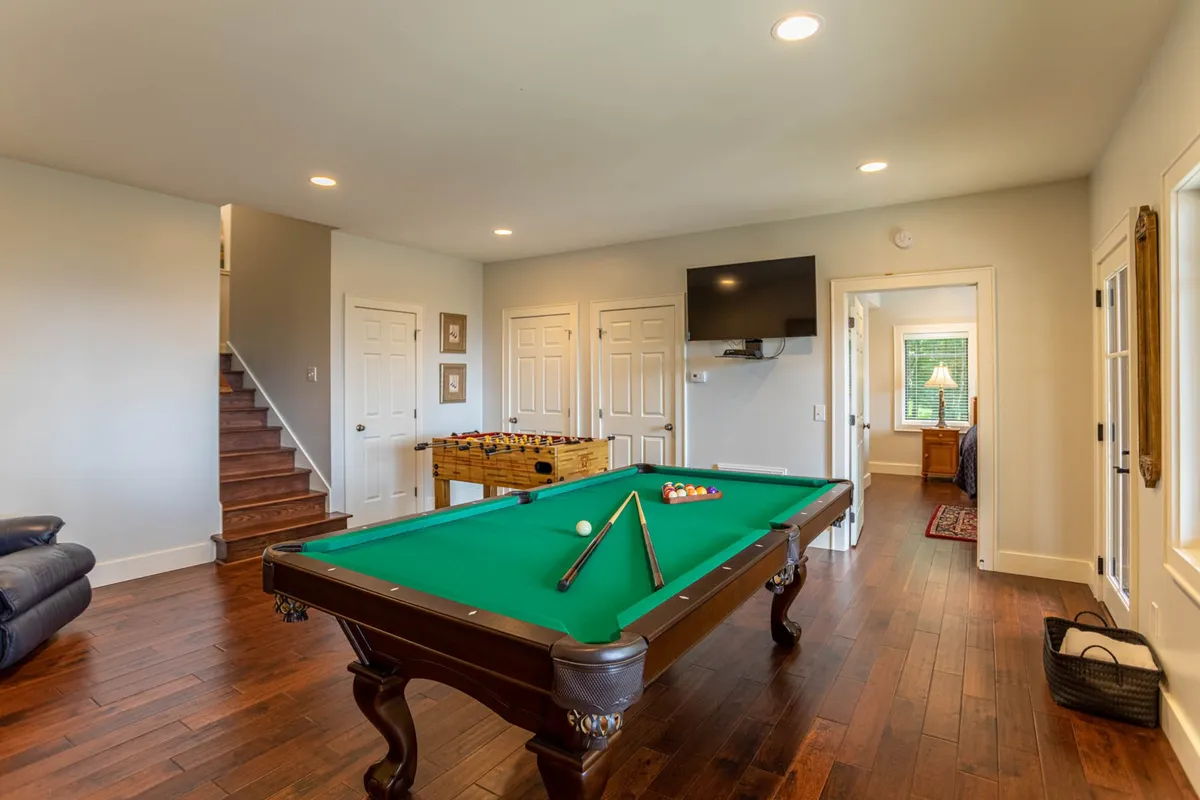 A lively game area with a pool table, foosball table, flat-screen TV, and stairs leading to the upper level. The mood is energetic and fun, perfect for friendly competition and casual lounging.