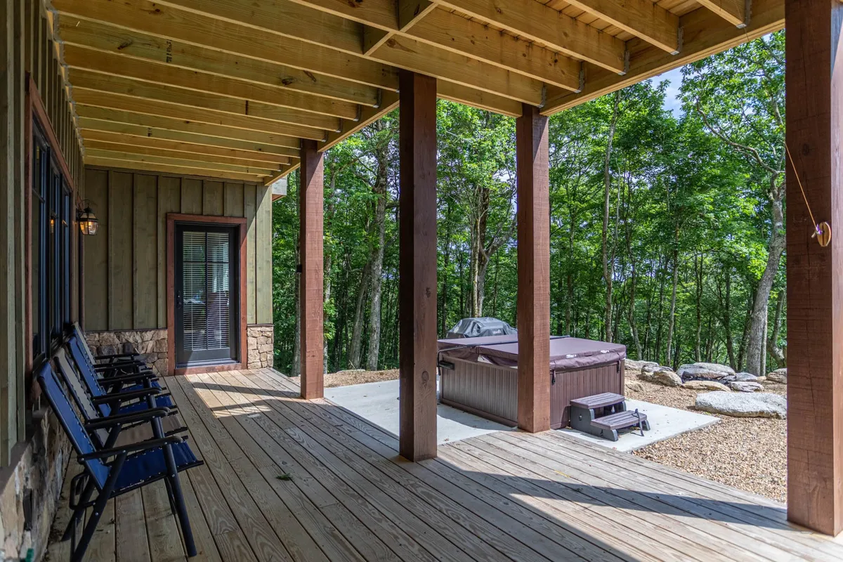 This image captures a spacious wooden deck surrounded by lush trees, with a hot tub prominently featured. The setting is tranquil and private, offering a perfect spot for relaxation and soaking while taking in the natural mountain environment.