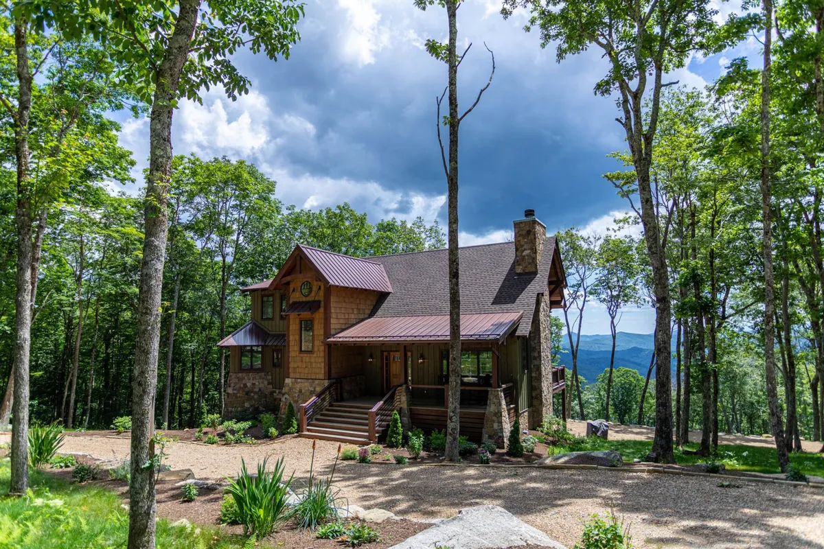 The hero image showcases a beautiful single-family mountain house framed by lush trees, with inviting stone steps leading up to a spacious porch—the perfect spot to watch sunsets and spot local wildlife.