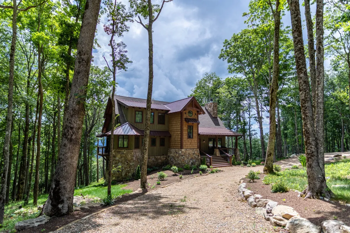 This exterior image features the house nestled among trees, with a gravel path leading through the natural landscape. The scene captures the inviting atmosphere of the mountain setting and hints at the easy outdoor access highlighted in the section. The presence of open spaces and the gravel path evokes the idea of walks with a pet and outdoor exploration.