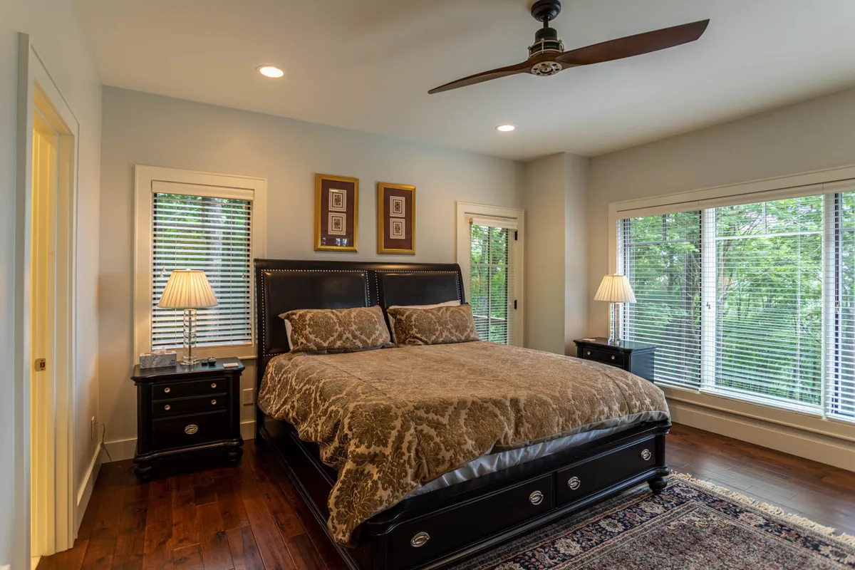 A serene master bedroom featuring a king-sized bed dressed in neutral bedding, flanked by nightstands with lamps. Large windows allow natural light to stream in, while decorative artwork adds a touch of elegance. The room exudes tranquility and privacy, ideal for restful nights.