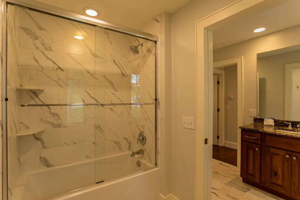 A spa-inspired bathroom featuring a spacious glass-enclosed shower, marble tile patterns, and a wooden vanity. The scene exudes serenity, inviting guests to unwind with relaxing self-care rituals after a long day.